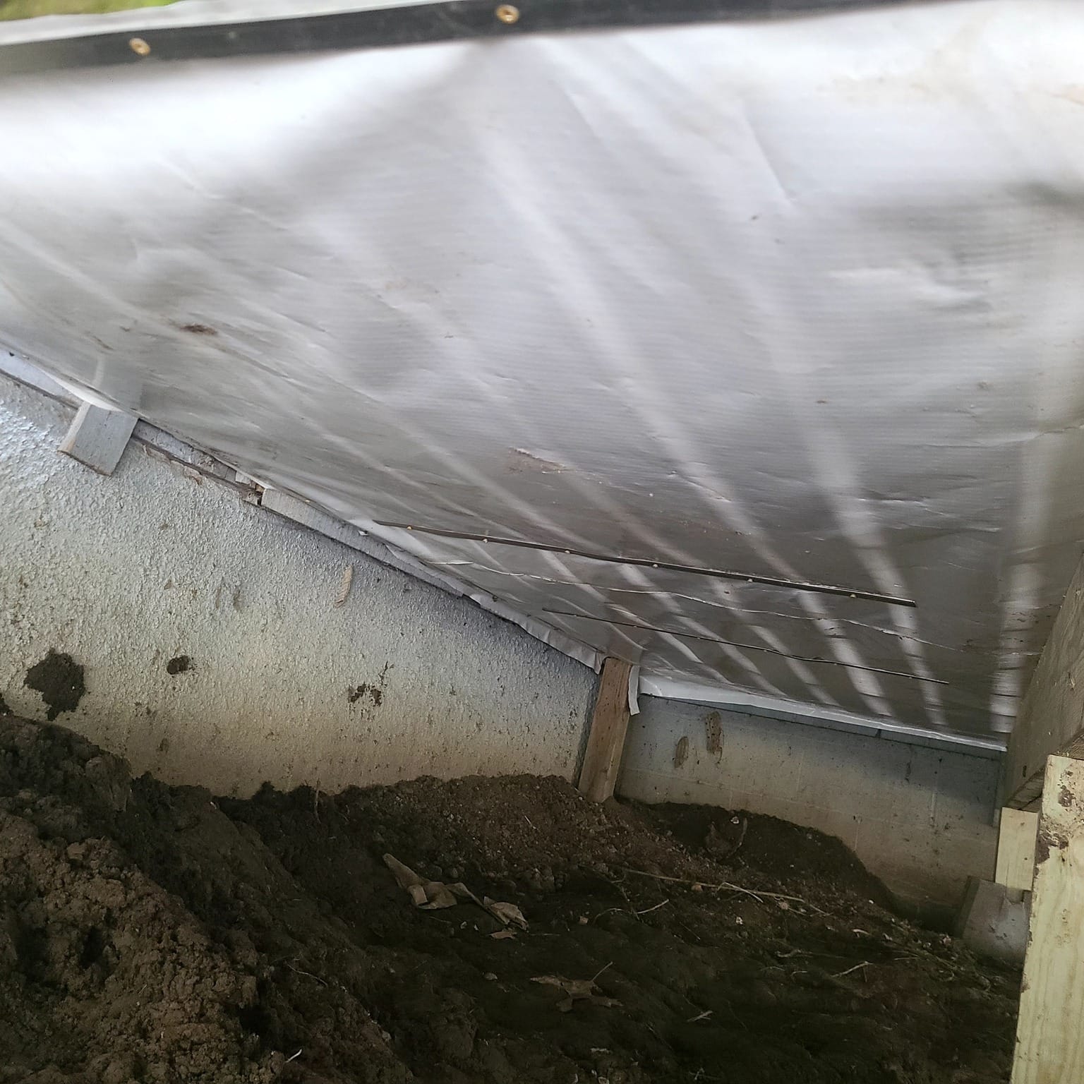 Basement wall lined with a white waterproofing vapor barrier